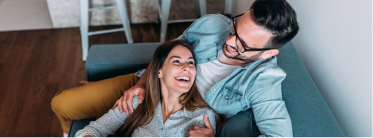 Vista desde arriba de un hombre y una mujer sentados en el sofá mientras se miran sonrientes.
